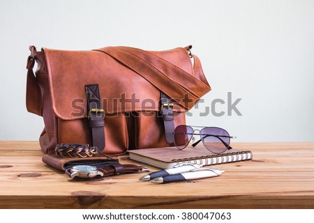 Brown leather bags with men\'s accessories on wooden table over wall background