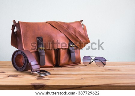 Men's accessories with brown leather bags, belt and sunglasses on wooden table over wall background