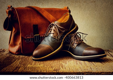 Men\'s accessories with brown shoes, leather bag and belt on wooden table over grunge background, still life style