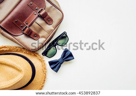 Men\'s accessories outfits with leather bag, sunglasses, hat, and bow tie, top view, flat lay on wooden board background