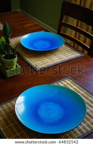 two dark blue plates sit on a dining room wood table on place mats