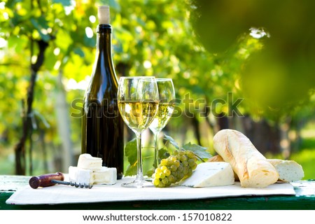 Two glasses of white wine, bottle, cheese and baguette