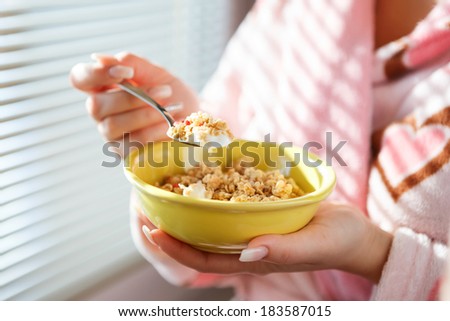 A close up shot of a woman holding a bowl of cereal and a raised spoon of cereal