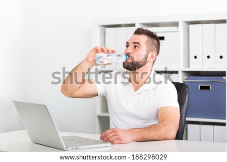 Handsome young man drinks water from a bottle in the office