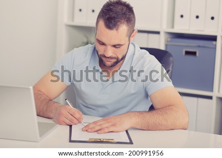 Young businessman in blue polo shirt signs a contract on white table, toned