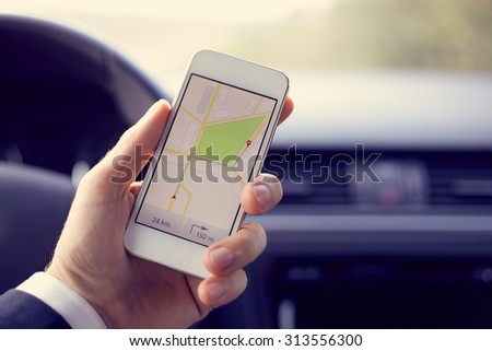 Man sitting in the car and holding white mobile phone with map gps navigation, toned