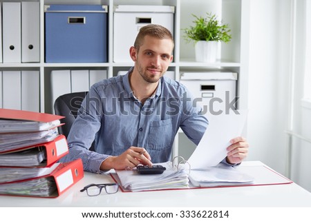 Young businessman calculates taxes at desk in office