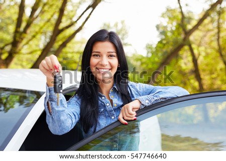 Happy woman driver showing car keys and leaning on car door