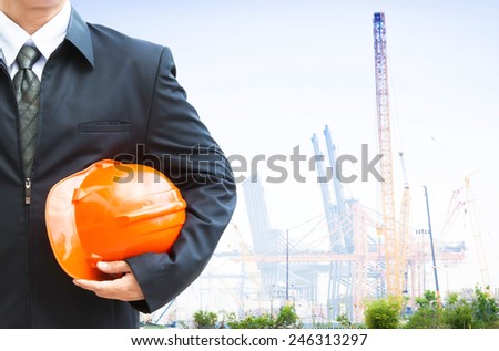 Engineer holding orange helmet for workers security on background  construction cranes and crane lifts load