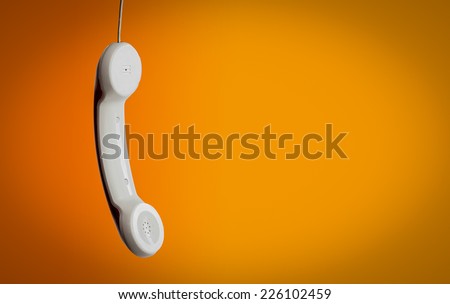 White handset telephone hanging against orange background