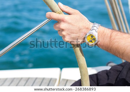 A man hand with a watch holding a sailing vessel wheel