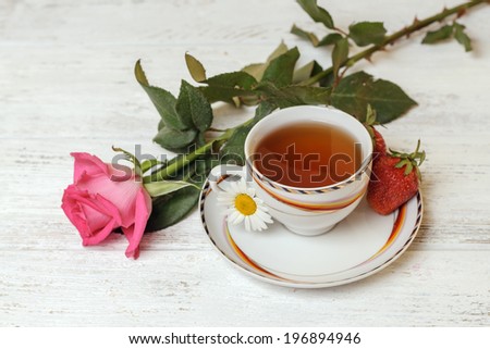 White cup of tea on the table with rose and strawberries