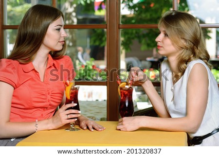 Two girls talking at a cafe table. Girls drink cherry juice sitting by the window