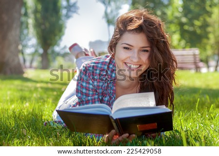 Beautiful girl with book in the summer park. Girl lying on the grass and reading a book
