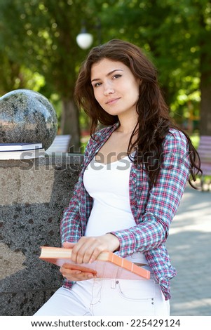 Girl holding a book in her hands. Student dressed in a plaid shirt and white jeans.