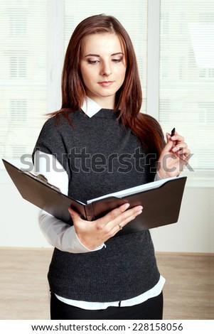Secretary girl holds a black folder open in one hand and in the other she holds a pen