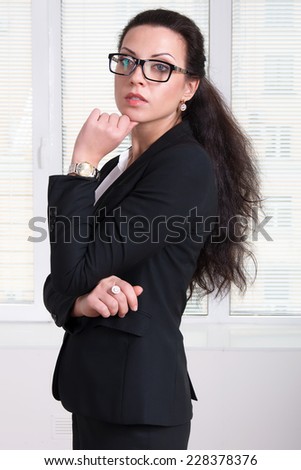 Woman leader in black business suit and glasses standing turned aside and propping up her hand chin