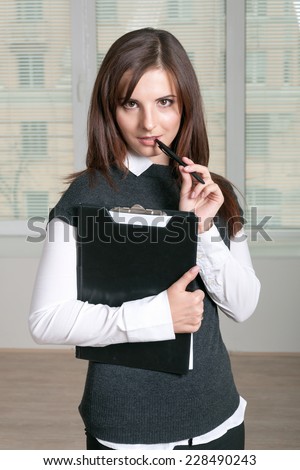 Girl holds a folder and puts a hand with a pen to her mouth