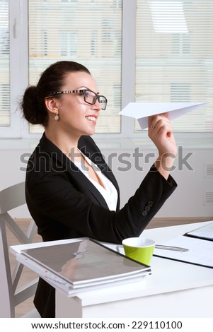 Business woman in a suit sitting at table in office throwing paper airplane