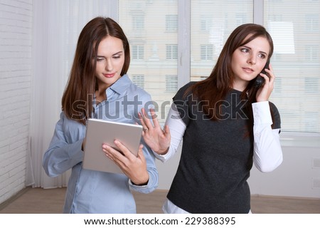 Two women in formal clothes standing back to back. One calls on the phone and other information found in her tablet