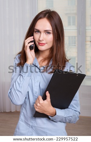 Girl in formal attire holding a folder and speaks by phone