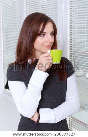 Woman drinking coffee near the window smiling and looking at the street