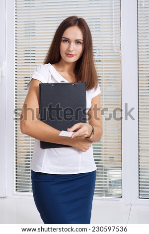 The girl with the folder in her hand a business card holds out against the window