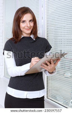 Woman in formal clothes writes in the folder standing at the window