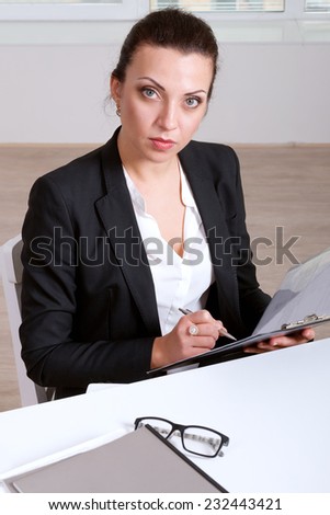 Girl in formal clothes writes in a folder sitting at the table
