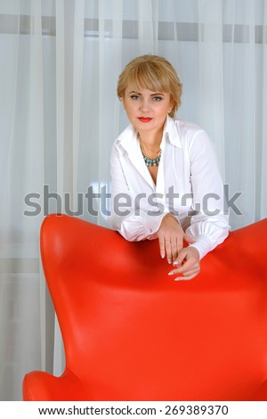Concept a confident business woman, leader, who stands behind the red chair against a light background