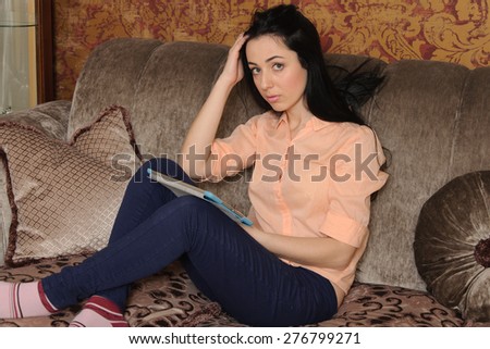 Woman in casual clothes sitting on the couch reading her pad thoughtful.