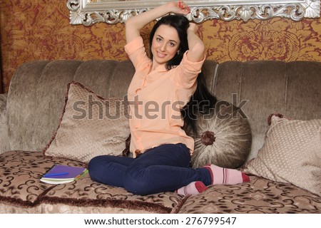 Woman in casual clothes sitting on a couch and stretches. Next to her is her diary for records.