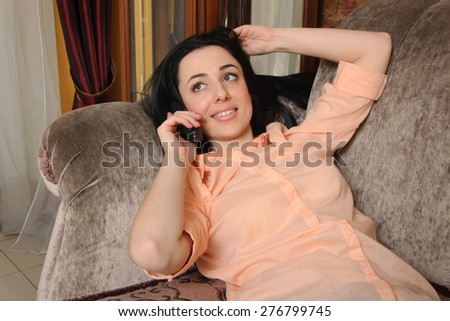 Woman in casual clothes lying on the couch and talking on the phone smiling and looking up