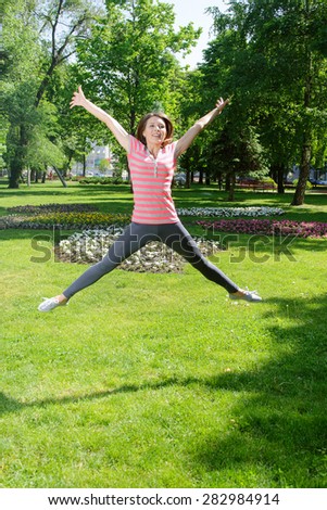 Girl makes a jump exercise outdoors at park against the backdrop of greenery