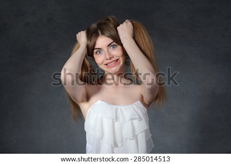 Irritation, anger, jealousy concept. Woman holds her hair against a dark gray background