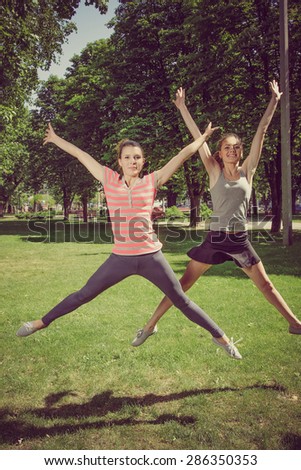 Two girls doing sport exercises in the form of synchronous jumps up on outdoors