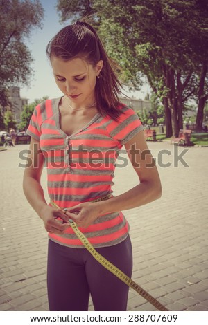 Slim girl in a red shirt measuring waist tape