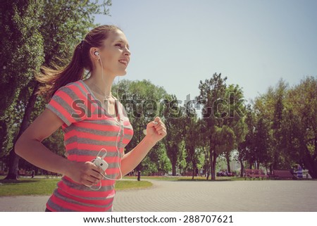 Sport woman running and listening to music with headphones in the phone outdoors against the sky