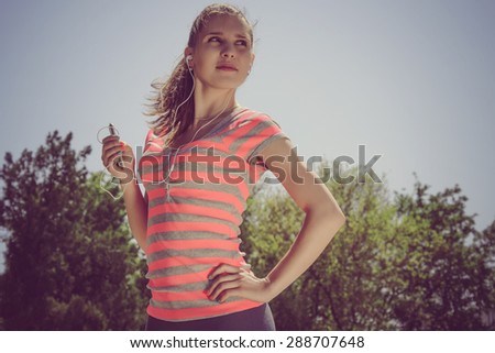 Sport woman in red shirt listening to music with headphones in the phone outdoors against the sky