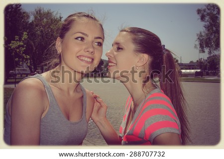 One girl tells another secret whisper in her ear. Both girls laughing