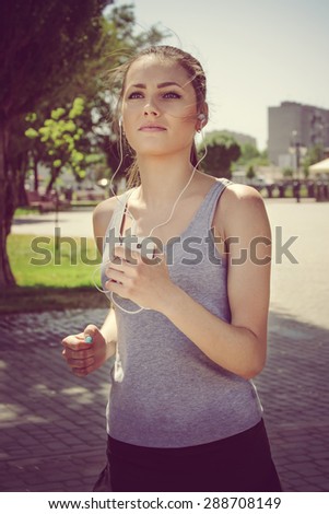 Sport woman running and listening to music with headphones in the phone in the park outdoors