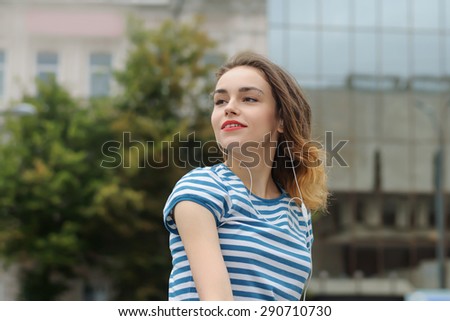 Serenity, freedom, pleasure concept. Girl in striped t-shirt listening to music in the background of the city