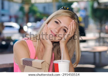 Subject fast food. Girl sitting in an outdoor cafe and smiles against a dark background