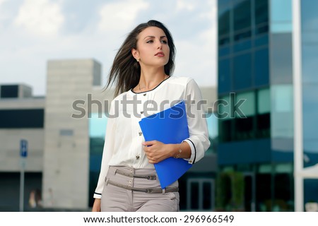 Business woman in formal clothes is on the city\'s business district with blue folder in her hand