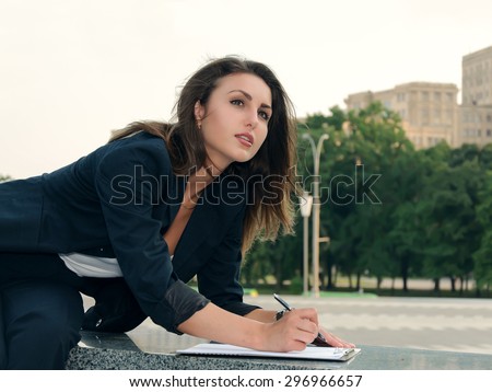 Business woman in formal clothes is on the city\'s business district makes notes in her business papers