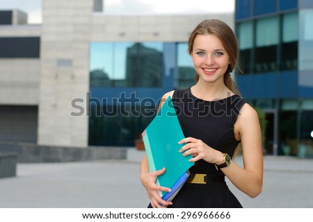 Business female in formal clothes is on the city\'s business district with folders for papers in her hands