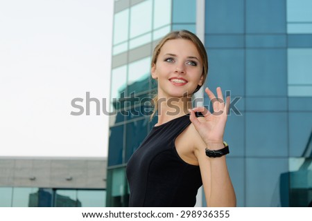Business woman in formal clothes shows gesture ok against the facade of a modern building