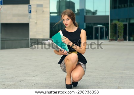 Business woman lifts off the ground folders with documents near the office building