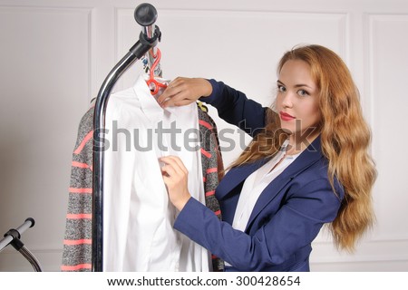 Woman in formal clothes takes his shirt off the rack at a clothing store against a light background