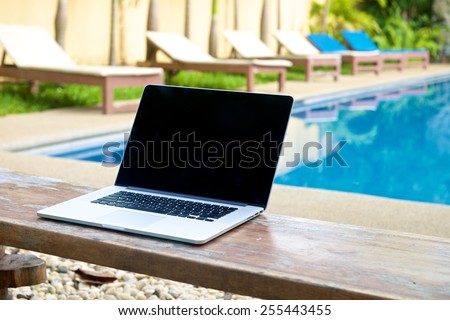 Laptop on a bench by the pool, working on vacation with mobility concept